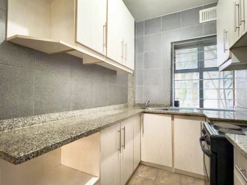 A functional kitchen featuring granite countertops, ample built-in cabinetry, a stainless steel sink, and tiled wall finishes.