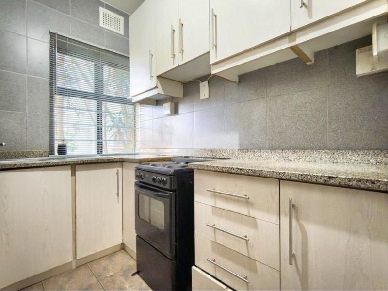 A functional kitchen featuring granite countertops, tiled backsplash, and ample built-in cabinetry with a freestanding stove.