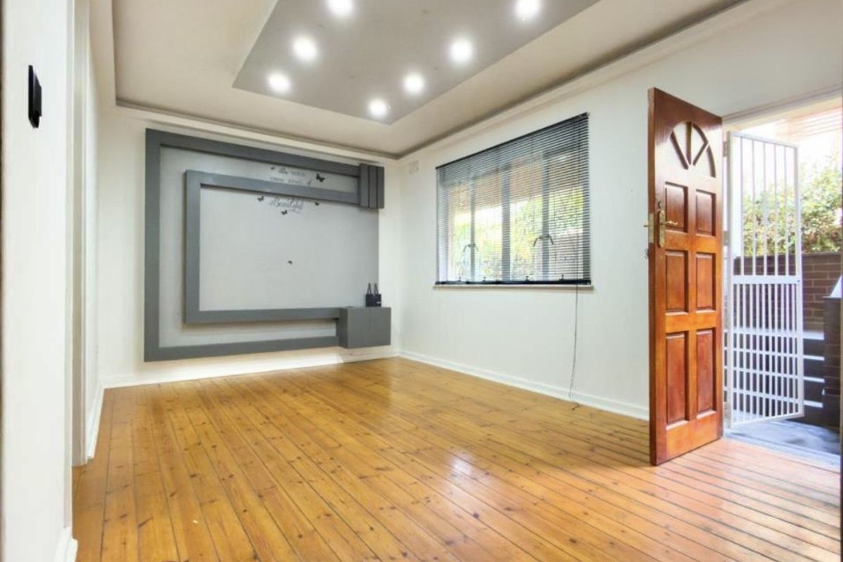 A bright, empty living room featuring polished timber flooring, a modern recessed ceiling with downlights, and a decorative built-in wall feature.