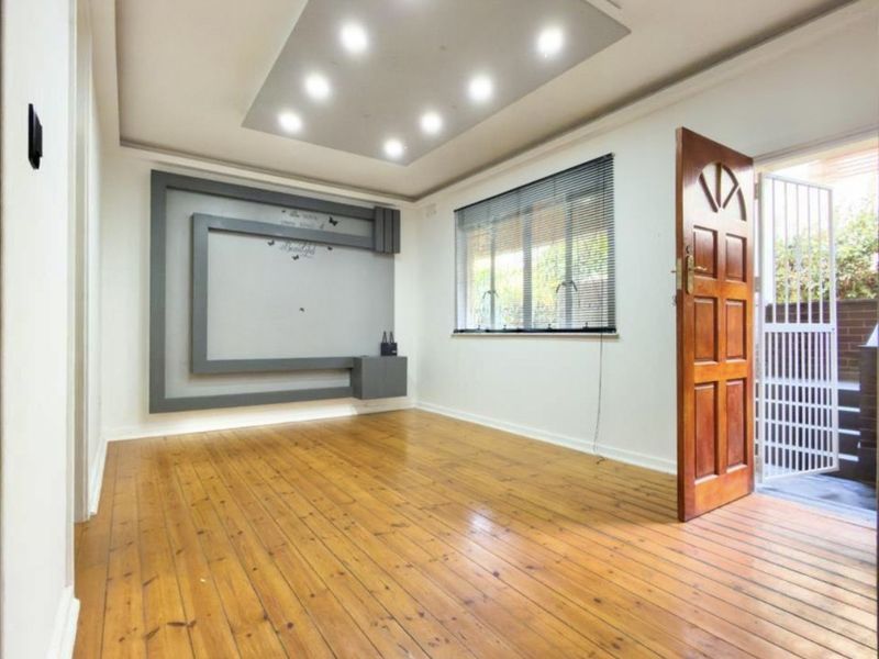 A bright, empty living room featuring polished timber flooring, a modern recessed ceiling with downlights, and a decorative built-in wall feature.