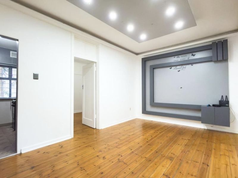 A bright, empty living room featuring polished hardwood flooring, a modern recessed ceiling with integrated lighting, and a custom built-in media wall unit.