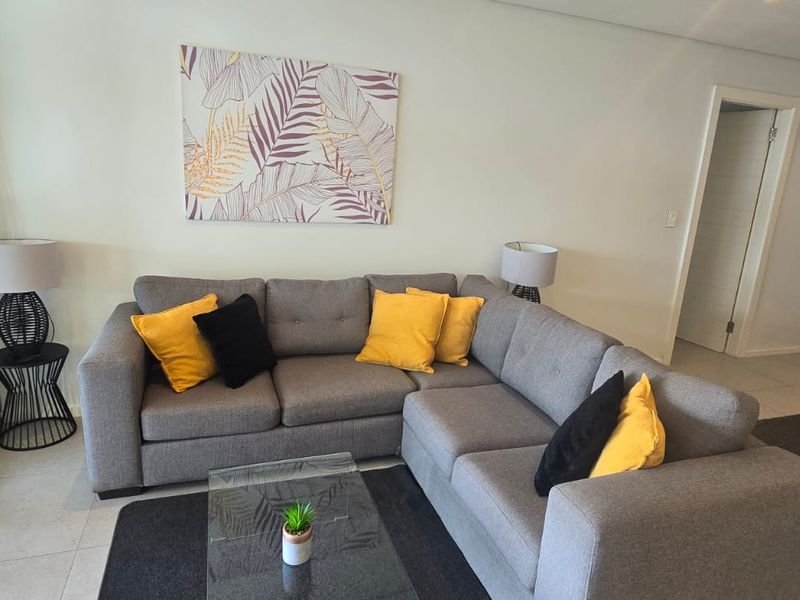 A well-maintained living room featuring neutral tiled flooring, recessed lighting, and large sliding glass doors providing access to an outdoor area.