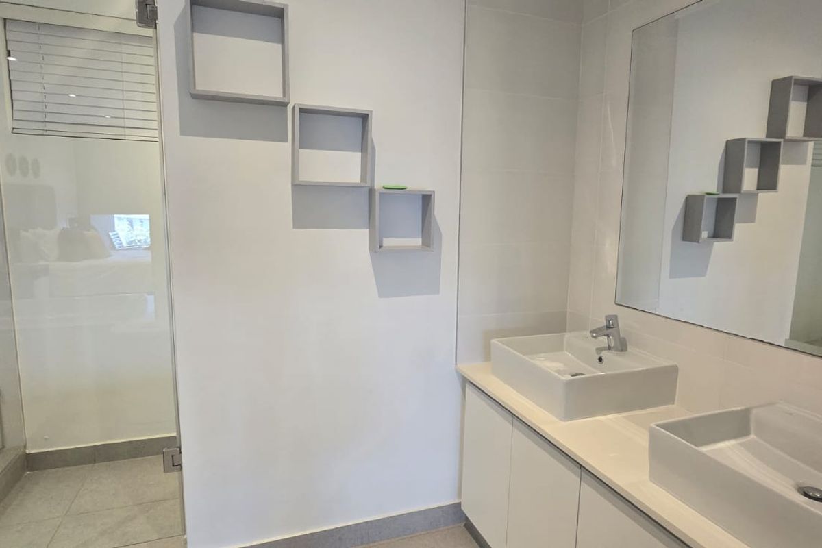 Modern bathroom featuring a double vanity with vessel sinks, chrome fixtures, a large wall mirror, and a glass-enclosed shower with tiled finishes.
