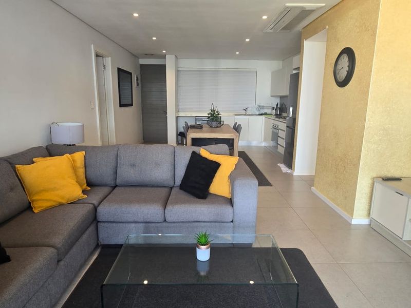 An open-plan living and kitchen area featuring tiled floors, recessed lighting, ducted air conditioning, and a textured feature wall.