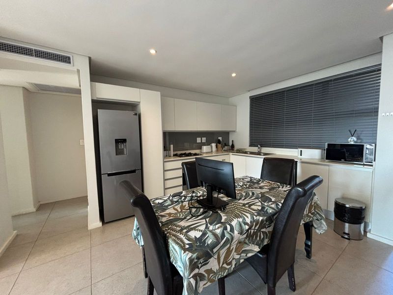 Modern open-plan kitchen and dining area featuring sleek built-in cabinetry, tiled flooring, ducted air conditioning, and contemporary finishes.