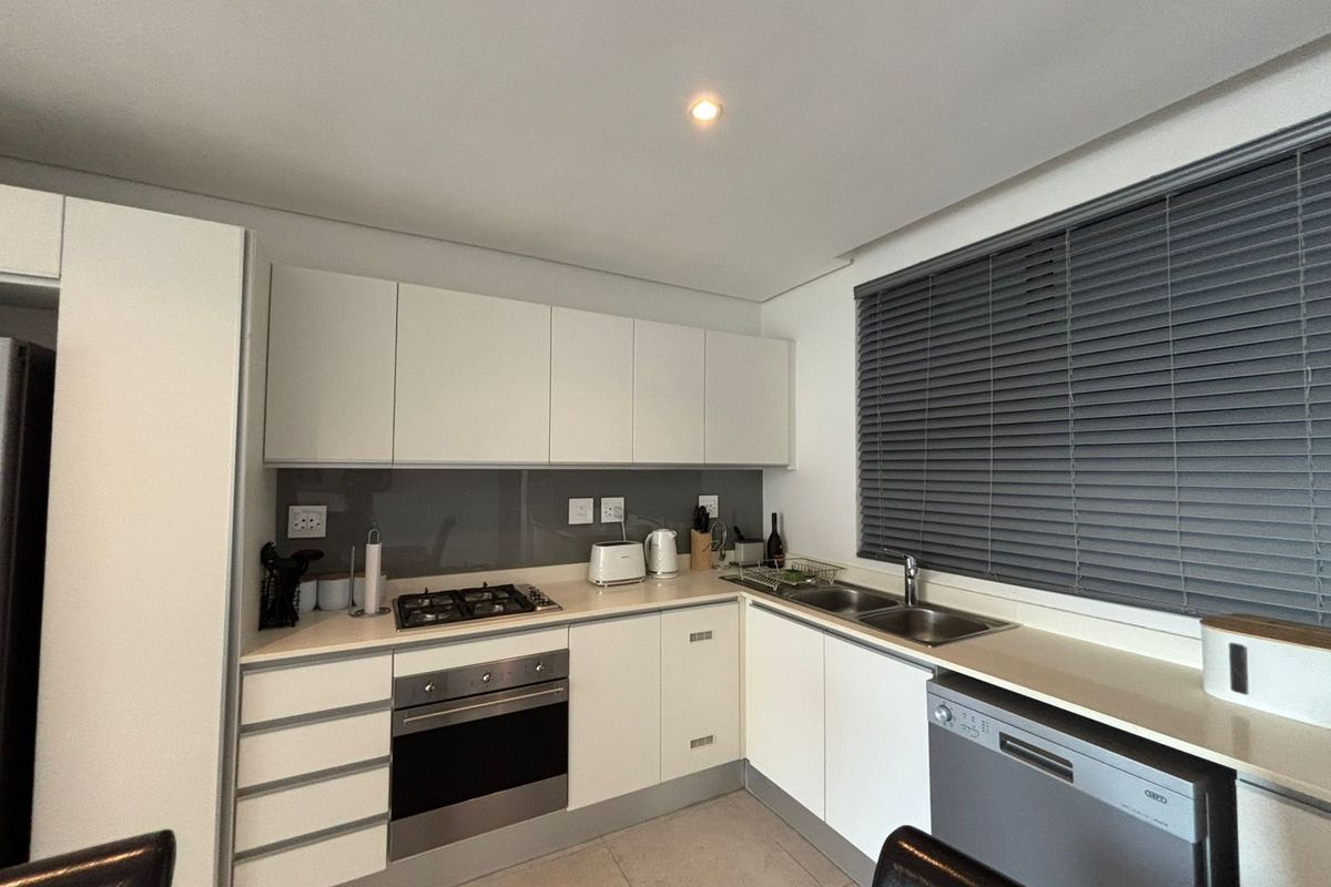 Modern kitchen featuring white cabinetry, gas hob, electric oven, stainless steel sink, and sleek glass splashback with neutral tiled flooring.
