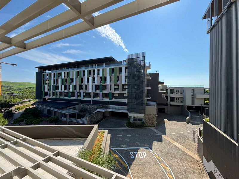 An elevated view of the modern apartment complex exterior, featuring contemporary architectural design, stone accents, and a paved visitor parking area.