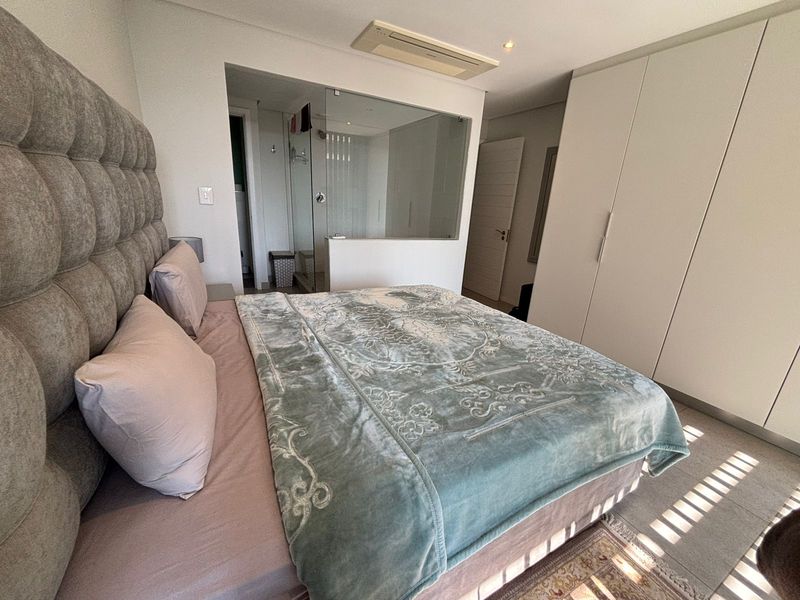 Modern bedroom featuring built-in cupboards, ducted air conditioning, and an open-plan en-suite bathroom with a glass partition.