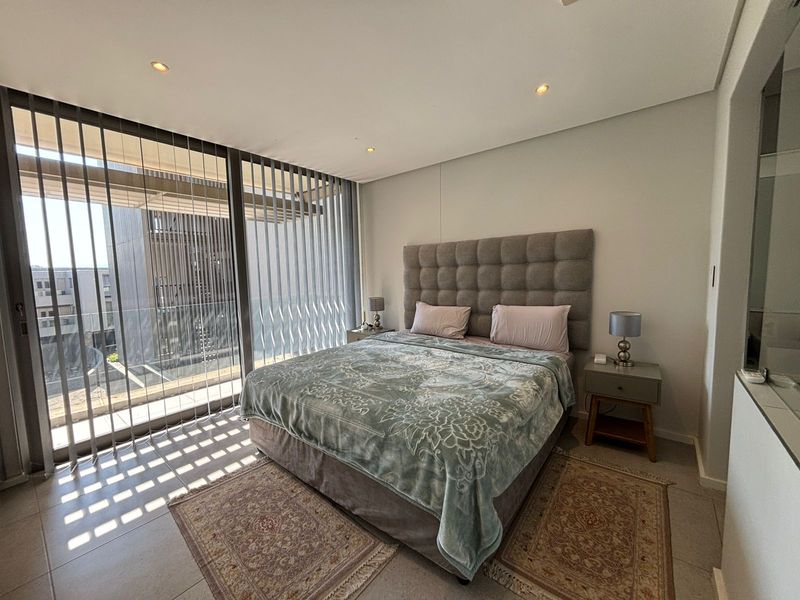 A modern bedroom featuring tiled flooring, recessed downlights, and a large sliding glass door with vertical blinds leading to an outdoor area.