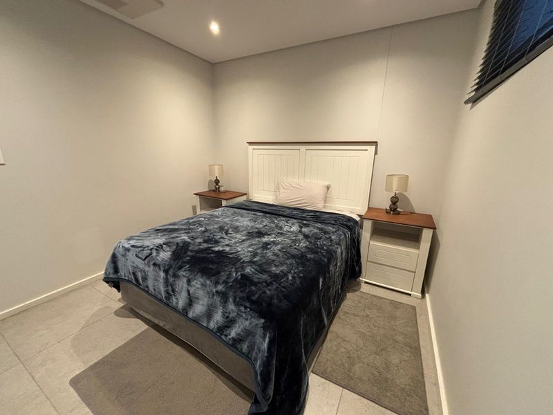 A clean, neutral bedroom featuring tiled flooring, recessed lighting, and modern venetian blinds, offering a simple and functional living space.
