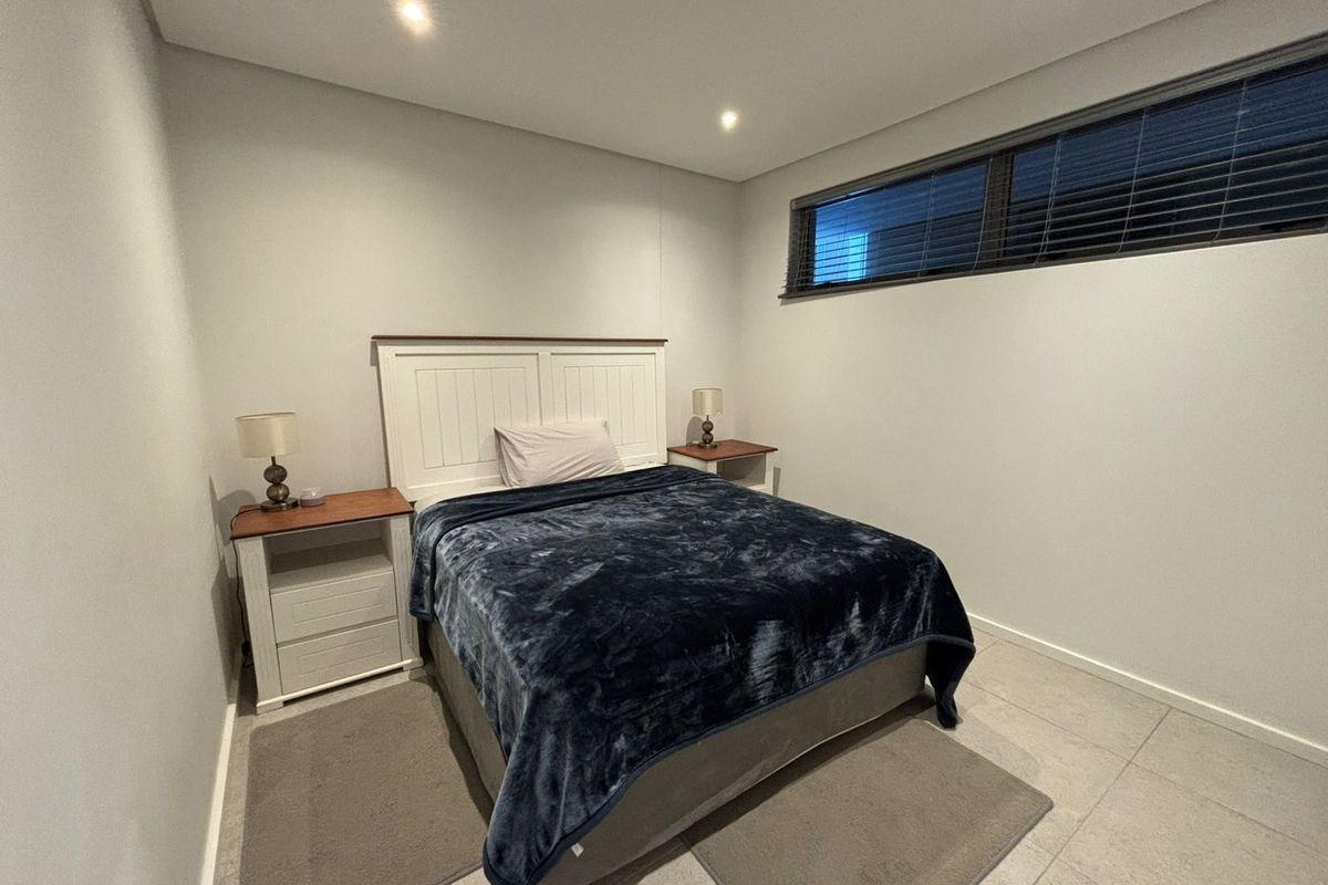 A clean and modern bedroom featuring neutral tiled flooring, recessed downlighting, and a high-set horizontal window with fitted blinds.