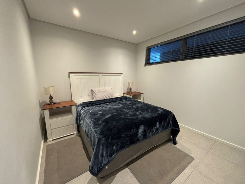A clean and modern bedroom featuring neutral tiled flooring, recessed downlighting, and a high-set horizontal window with fitted blinds.