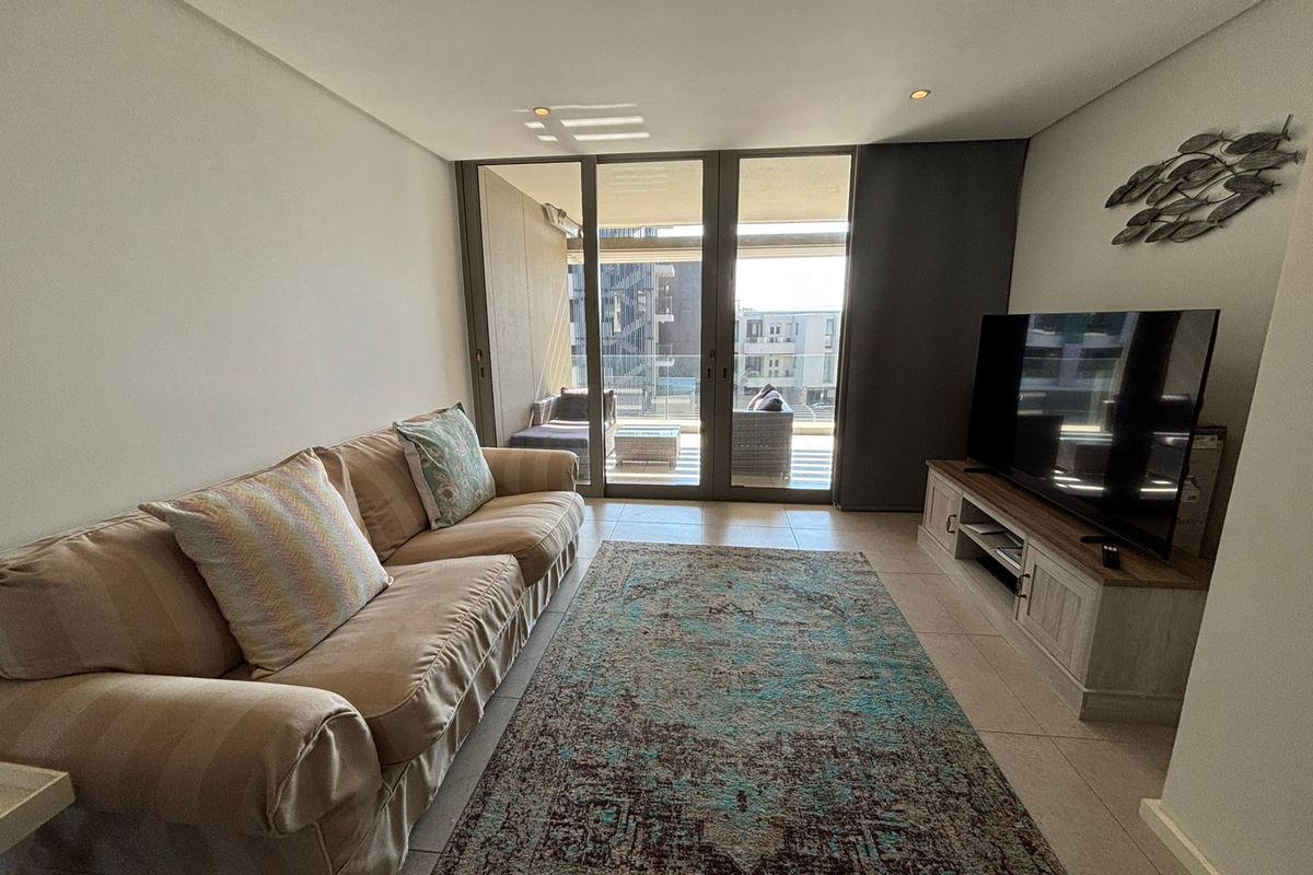 A bright living room featuring tiled floors, recessed lighting, and large sliding glass doors that open onto a private balcony.