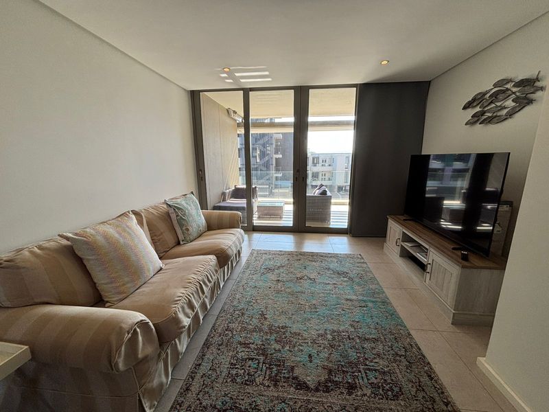 A bright living room featuring tiled floors, recessed lighting, and large sliding glass doors that open onto a private balcony.