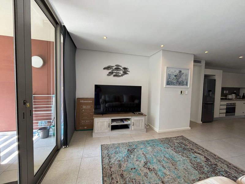 Modern open-plan living area featuring tiled floors, recessed lighting, and seamless access to an outdoor balcony, flowing into a contemporary kitchen space.