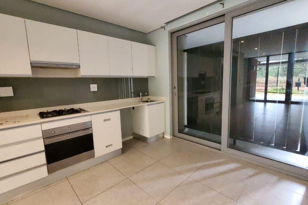 Modern kitchen featuring white cabinetry, stone countertops, integrated gas hob and oven, with large sliding doors providing access to the outdoor area.