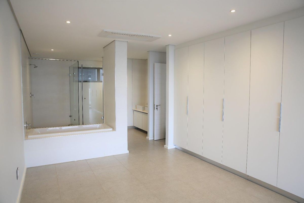A modern, spacious bathroom featuring a built-in bathtub, glass-enclosed shower, vanity area, and extensive built-in wardrobe storage with a clean, minimalist aesthetic.