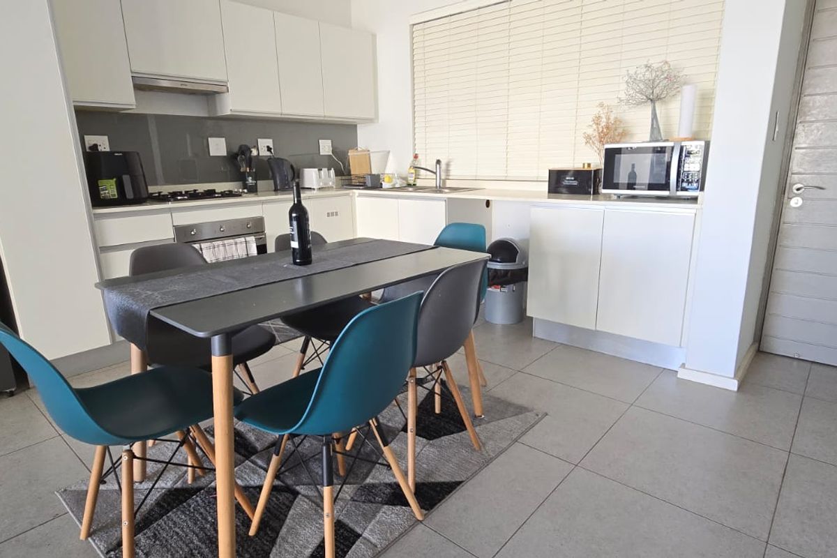 Open-plan kitchen and dining area featuring modern white cabinetry, tiled flooring, and integrated appliances, creating a functional and bright living space.