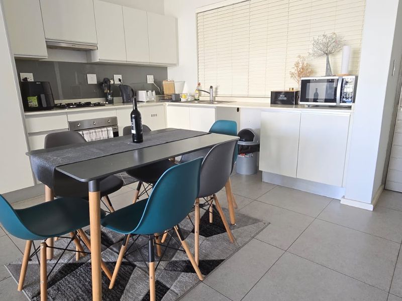 Open-plan kitchen and dining area featuring modern white cabinetry, tiled flooring, and integrated appliances, creating a functional and bright living space.