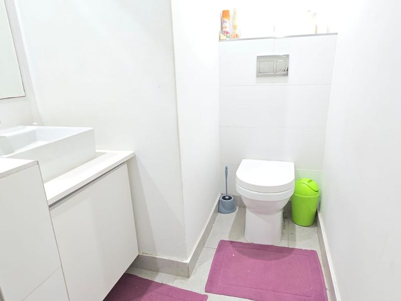 A clean, modern bathroom featuring a wall-hung toilet with a concealed cistern, a vanity cabinet with a countertop basin, and a glass shower screen.