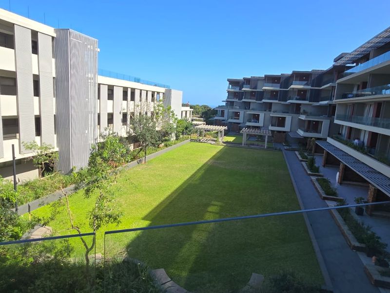 A view of the central landscaped courtyard and lawn area between modern apartment blocks, featuring glass balustrades and paved walkways.