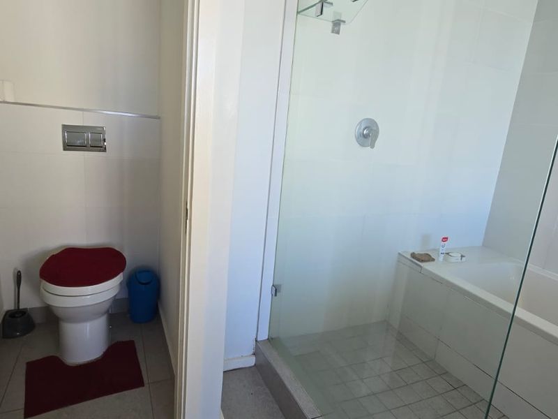 A modern bathroom featuring a wall-hung toilet with a concealed cistern, a glass-enclosed shower, and a built-in bathtub with clean white tiling.