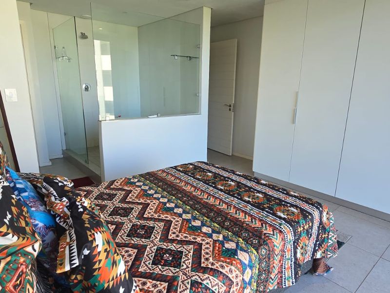 Modern bedroom featuring built-in cupboards, tiled flooring, and an en-suite bathroom with a glass-enclosed shower.