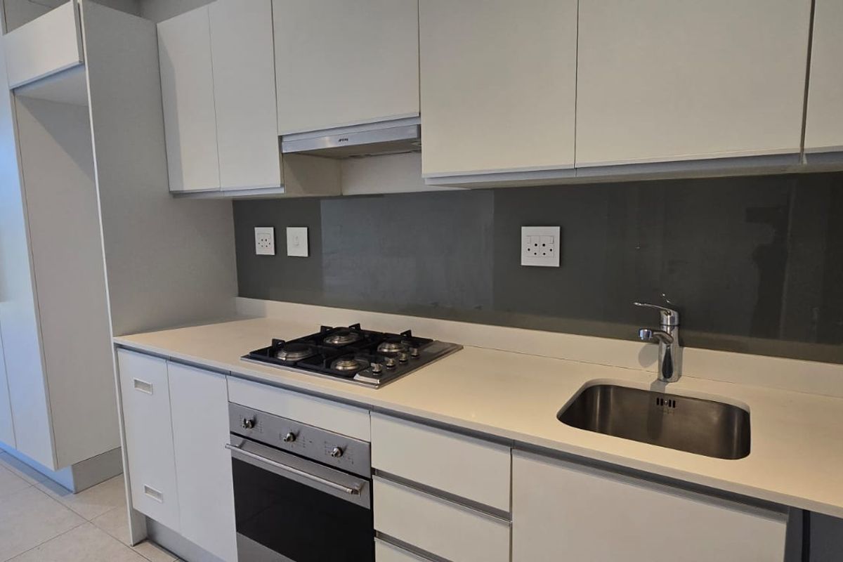 Modern kitchen featuring sleek white cabinetry, stone countertops, a gas hob, built-in oven, and a contemporary glass splashback.