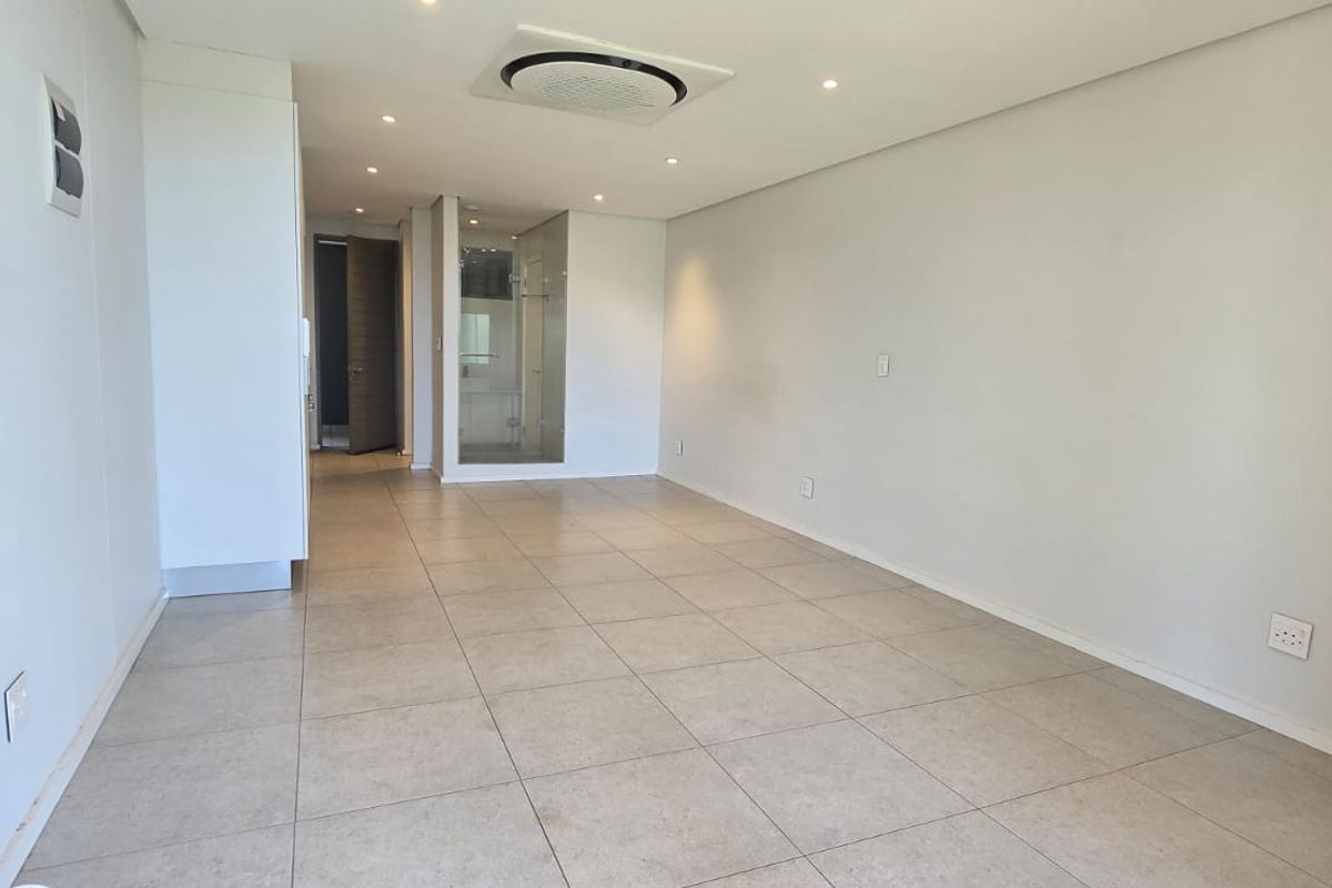A bright, open-plan living area featuring neutral tiled flooring, recessed ceiling lighting, and a modern ducted air conditioning system.