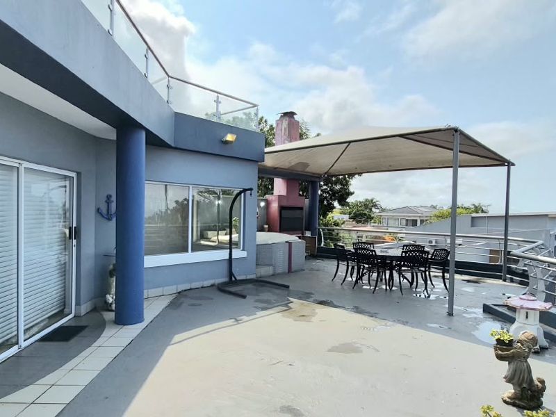 Spacious elevated balcony featuring a built-in braai, glass balustrades, and a covered outdoor entertainment area with views of the surrounding neighborhood.