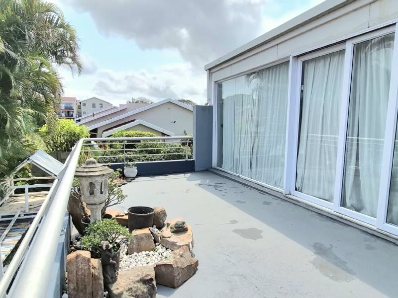 A spacious balcony featuring sliding glass doors, a metal safety railing, and a paved surface, offering an elevated outdoor area.