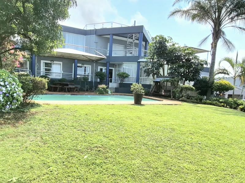 Rear view of a multi-story house featuring a swimming pool, paved patio, balcony, and a well-maintained garden.