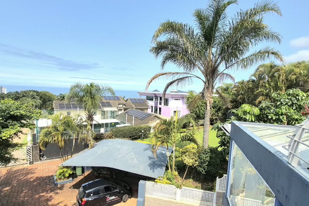 An elevated aerial view of the property grounds, featuring a paved driveway, carport, solar panel installations, and surrounding landscaped garden area.