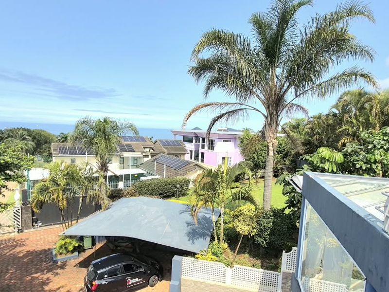 An elevated aerial view of the property grounds, featuring a paved driveway, carport, solar panel installations, and surrounding landscaped garden area.