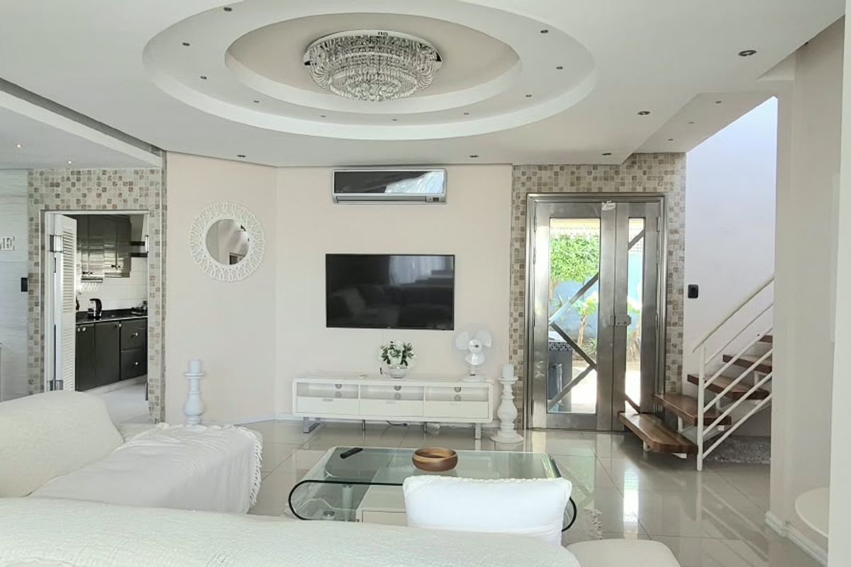Spacious living room featuring a decorative circular recessed ceiling with a crystal chandelier, tiled floors, and a modern staircase with metal railings.