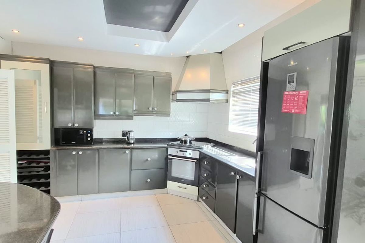 Modern kitchen featuring dark grey cabinetry, granite countertops, built-in oven, extractor fan, and recessed ceiling lighting with tiled flooring.