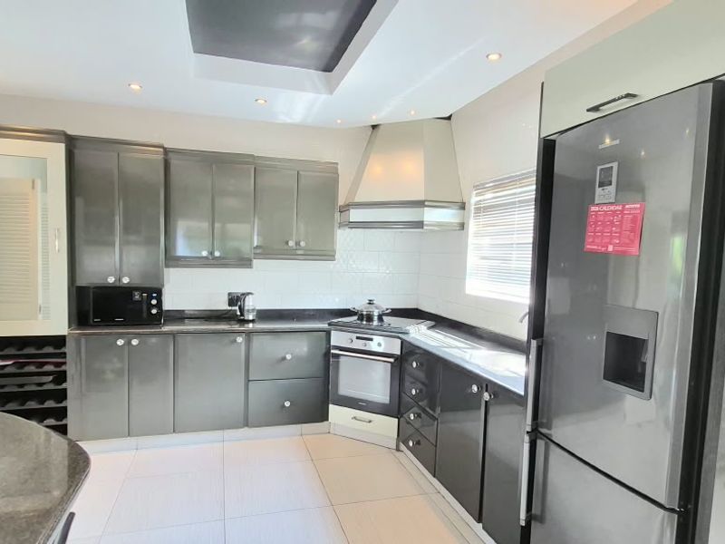 Modern kitchen featuring dark grey cabinetry, granite countertops, built-in oven, extractor fan, and recessed ceiling lighting with tiled flooring.
