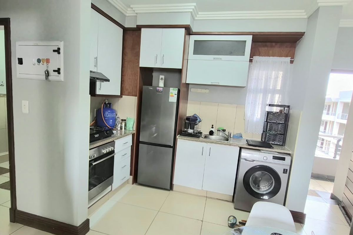 Compact kitchen featuring built-in cabinetry, integrated oven and hob, stainless steel sink, and tiled flooring, with direct access to an adjacent balcony area.