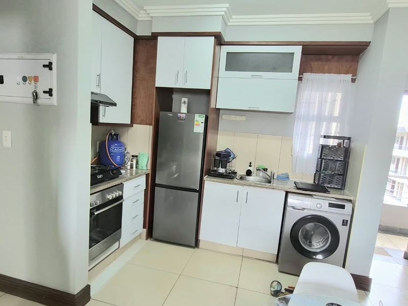 Compact kitchen featuring built-in cabinetry, integrated oven and hob, stainless steel sink, and tiled flooring, with direct access to an adjacent balcony area.