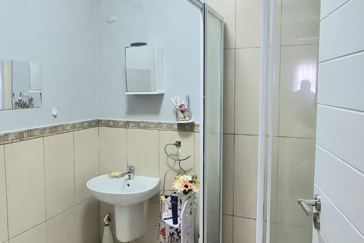 A functional bathroom featuring a pedestal basin, a glass-enclosed shower, and neutral wall and floor tiling.