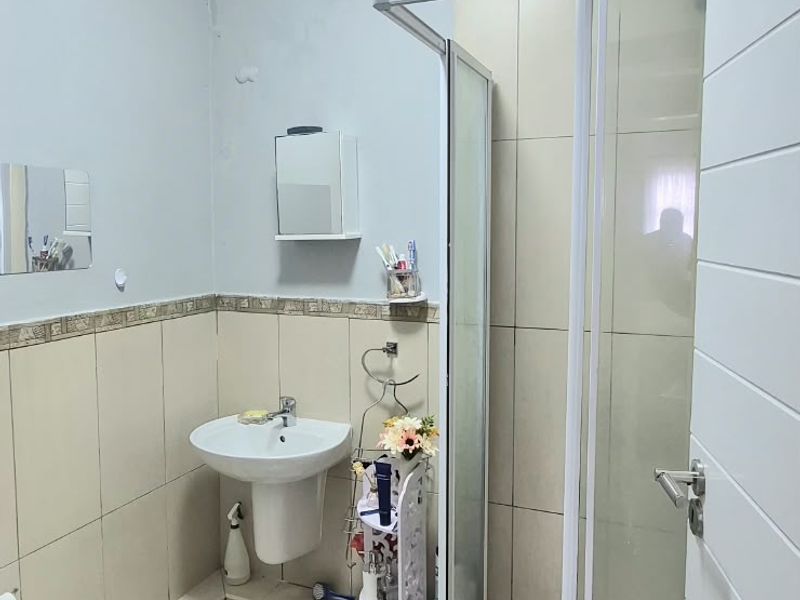 A functional bathroom featuring a pedestal basin, a glass-enclosed shower, and neutral wall and floor tiling.
