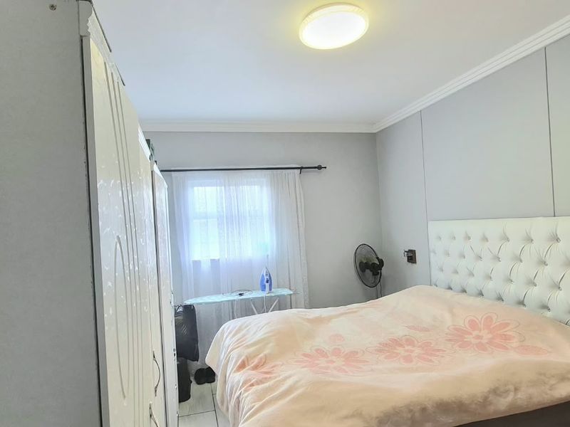 A functional bedroom featuring tiled flooring, coving, and a built-in wardrobe, providing a clean and neutral space for rest.