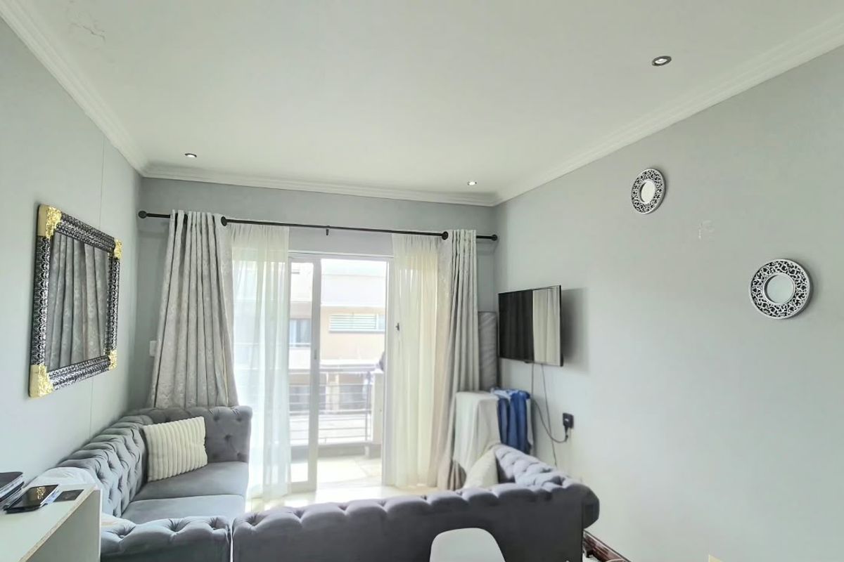 A well-lit living room featuring neutral walls, recessed ceiling lighting, and a sliding glass door providing access to an outdoor balcony area.