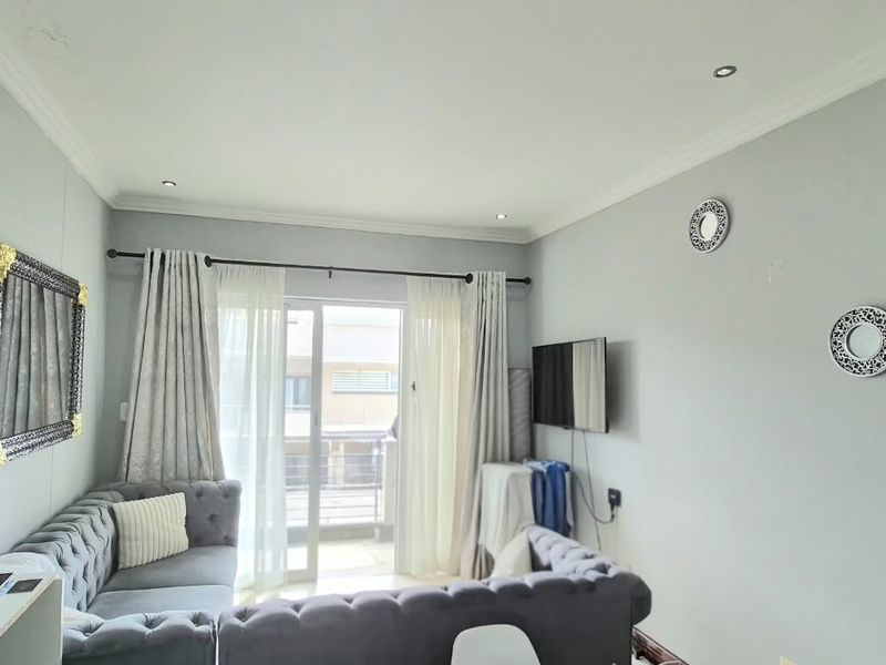 A well-lit living room featuring neutral walls, recessed ceiling lighting, and a sliding glass door providing access to an outdoor balcony area.