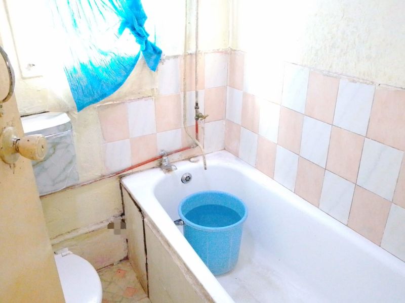 A dated bathroom featuring a standard bathtub, toilet, and tiled walls, currently requiring significant renovation and modernization of fixtures and finishes.