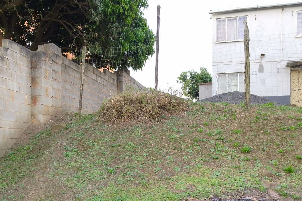 Rear exterior view of the property featuring a sloped garden area, concrete block boundary wall, and wire mesh fencing.
