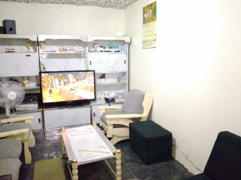 A living room featuring tiled flooring and a textured ceiling, currently showing signs of wear including wall cracks and peeling paint.