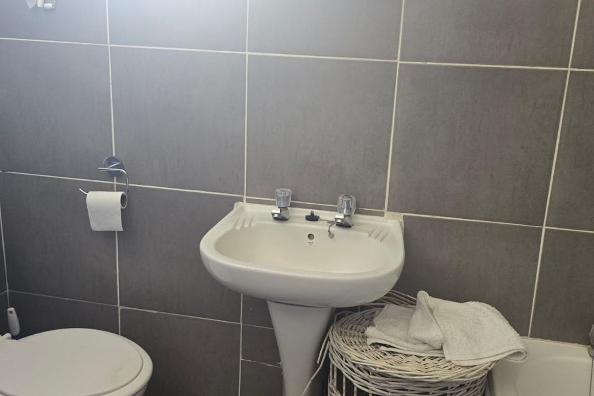 A functional bathroom featuring a pedestal basin, toilet, and bathtub with neutral grey wall tiling.
