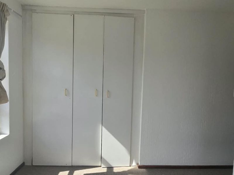 A bright, empty bedroom featuring built-in cupboards and large windows with natural light, offering a clean canvas for personalization.