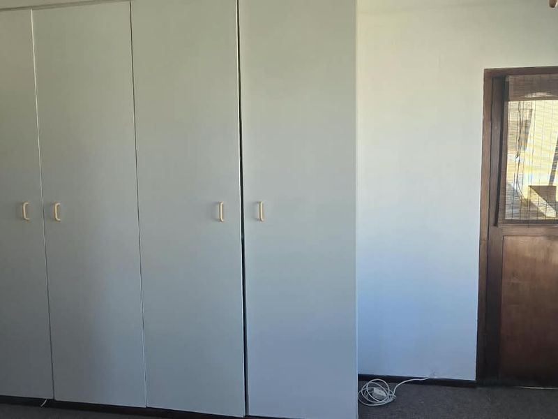 A bright, empty bedroom featuring built-in cupboards, a timber door, and natural light from the window.